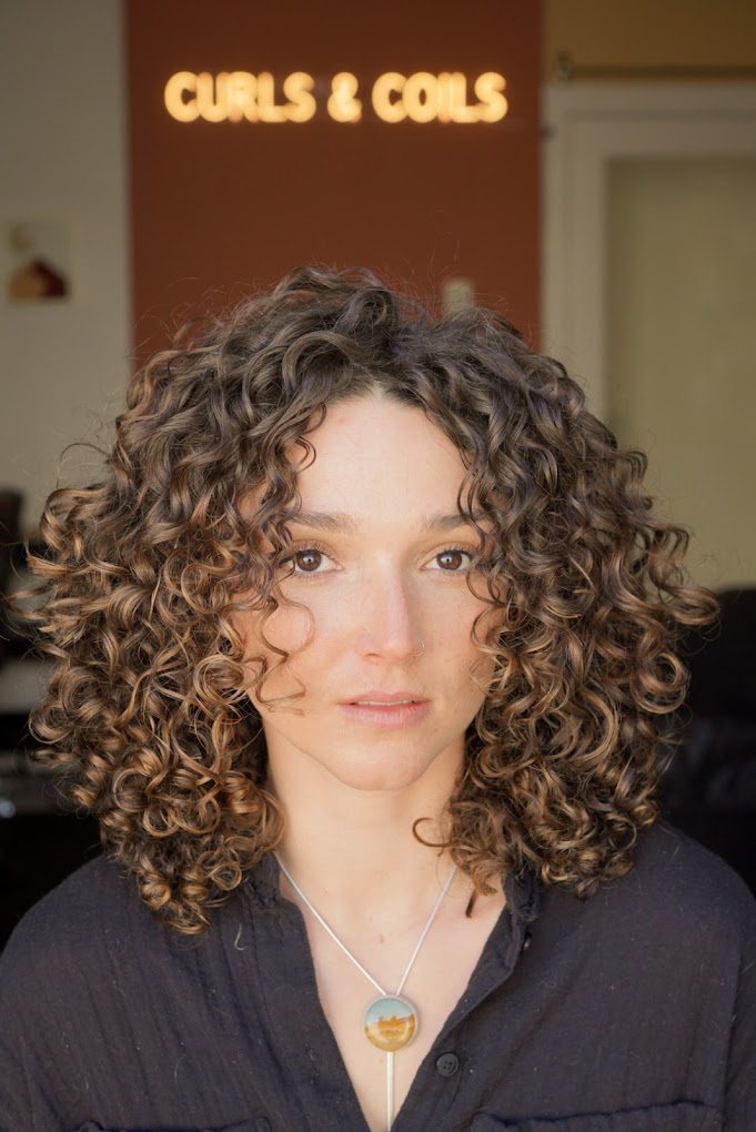 Guest with shoulder-length, defined brown curls in front of the Curls & Coils sign