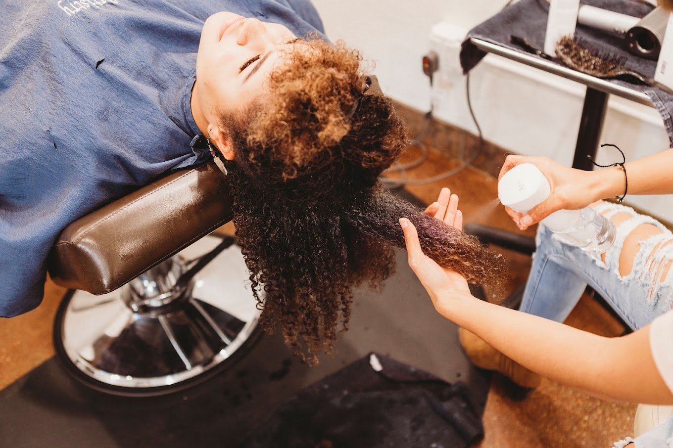 A guest reclined in the chair while a stylist mists her long, coily hair